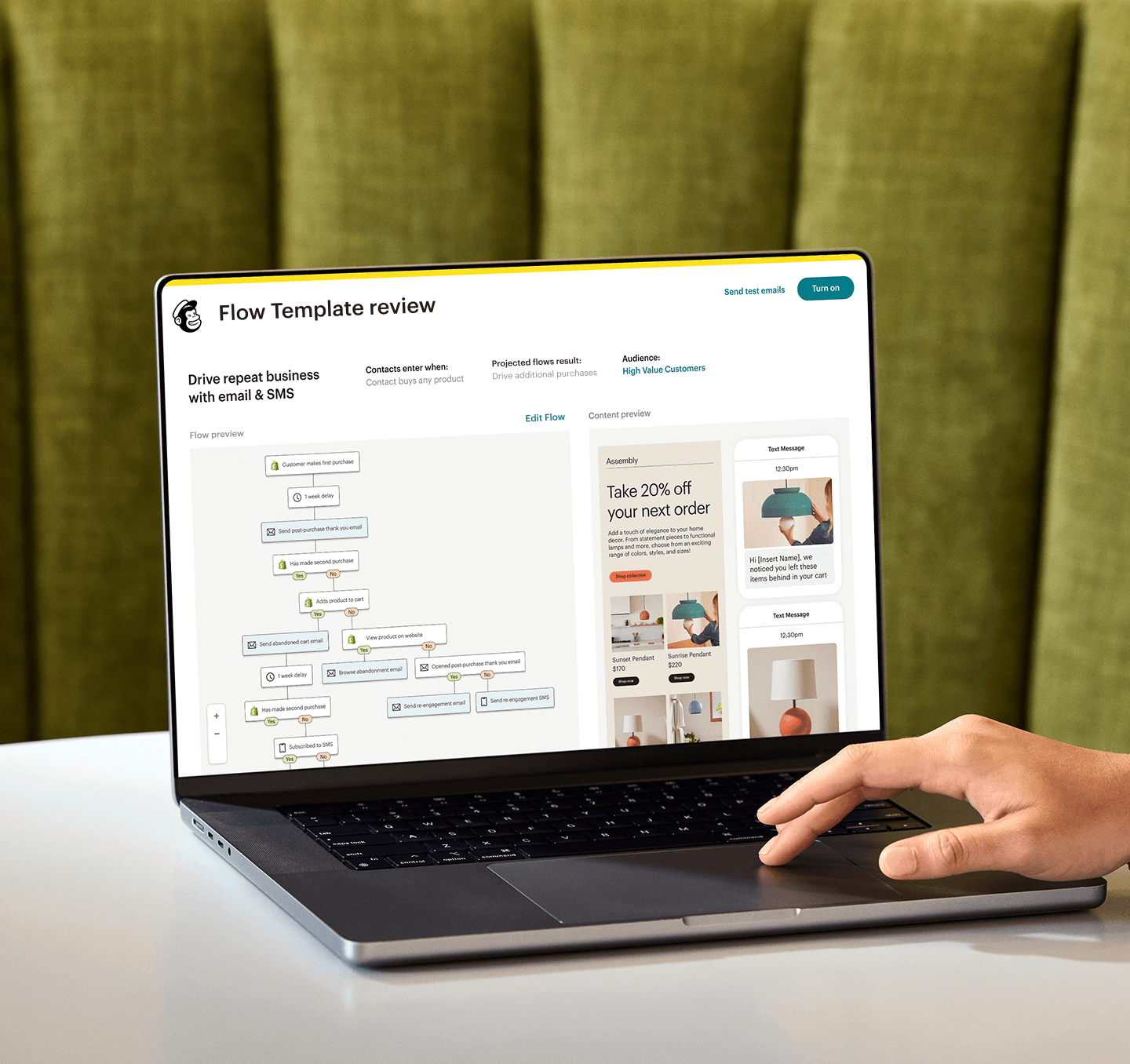 Image of a person sitting at a desk, looking at a laptop screen displaying Mailchimp’s Flow Template review feature. The feature shows a preview of an automation flow and an abstract view of email and SMS interfaces from the fictitious brand Assembly.